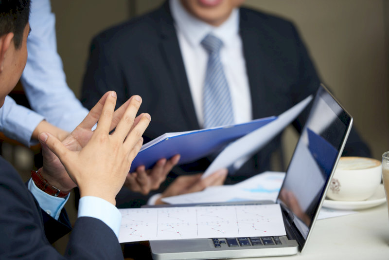 Tư vấn doanh nghiệp chuyên nghiệp, các cá nhân mặc vest đang trao đổi tài liệu và dữ liệu trên laptop trong cuộc họp.